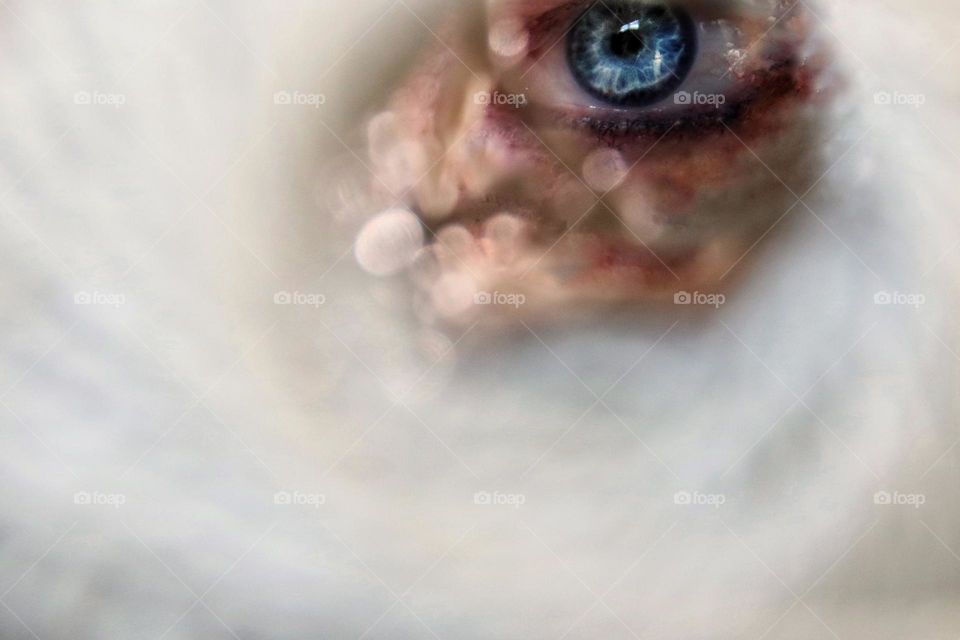 A woman's blue eye photographed through a ball of yarn