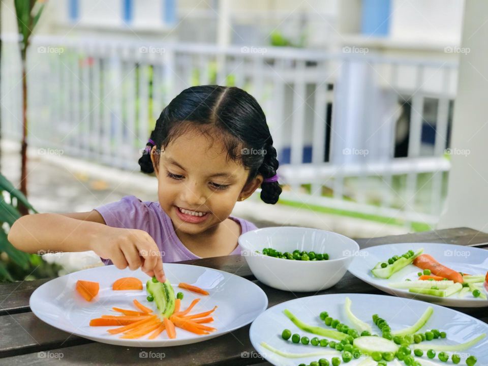 Girl making palm tree and sun shapes with the help of all vegetables like carrots green peas and bottle guard 