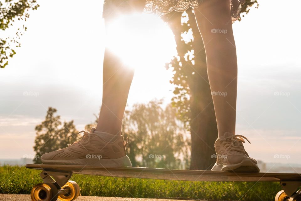 Crop faceless woman standing on longboard against sunset