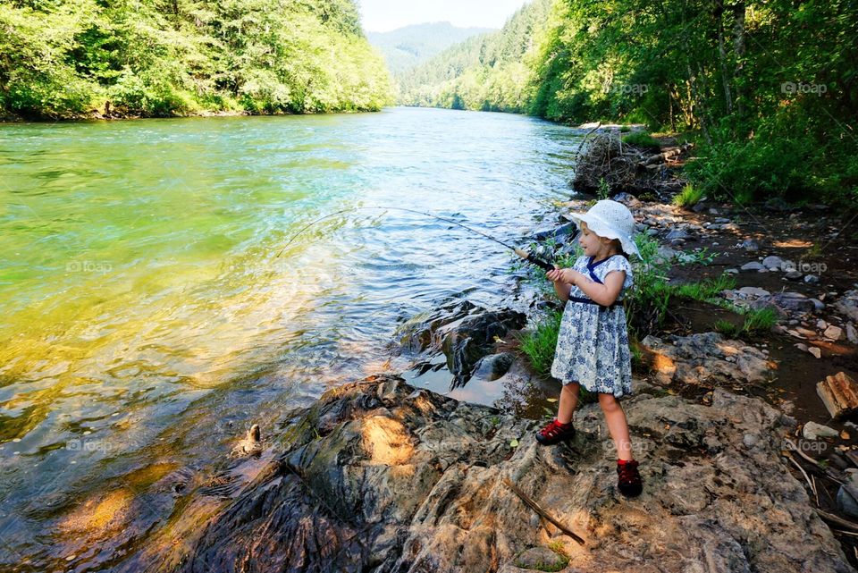 Little girl fishing in a dress standing on rocks by the river