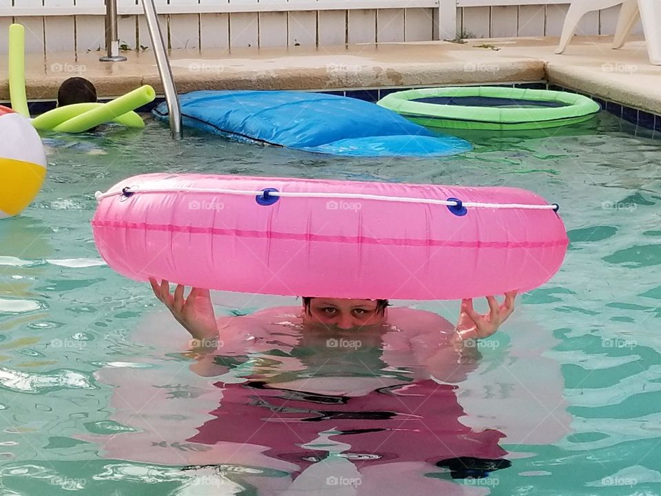 Kid posing with a pink pool float in the pool during summer