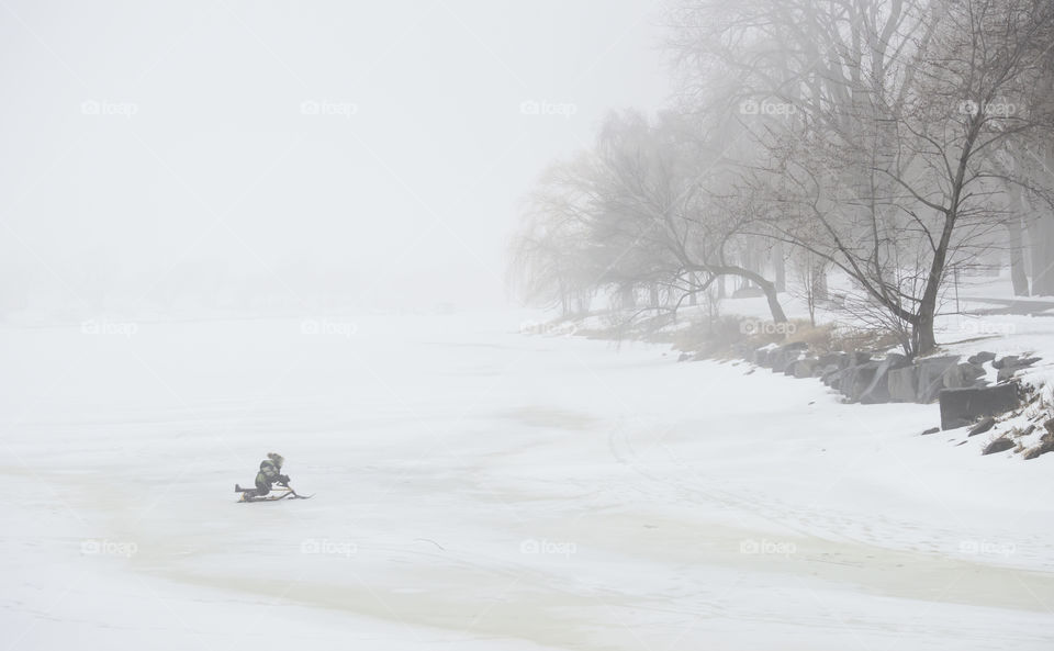 Foggy winter morning child sledding across frozen lake on winter day in thick fog winter landscape background 