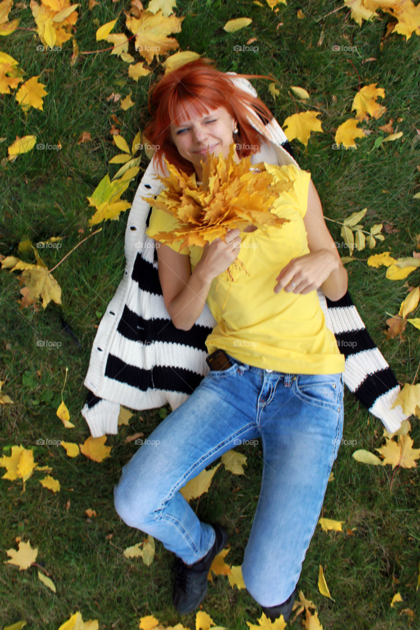 Woman lying on grass holding autumn trees in hand