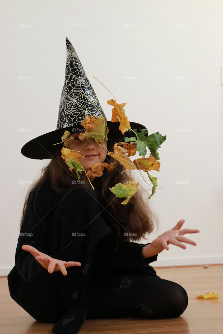 A girl in costume of witch is playing with leaves for Halloween 