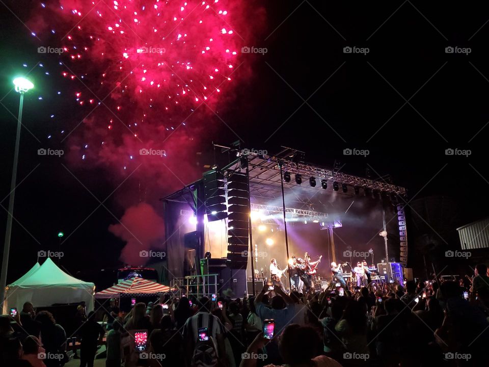 A crowd enjoying a nighttime concert and fireworks in celebration of Independence day in the United States of America.