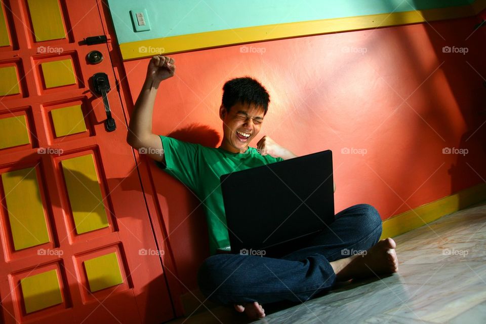 young asian teen with a laptop computer in a living room and happy