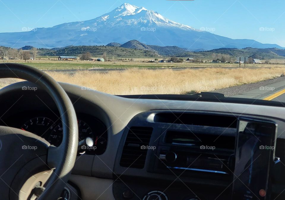 view of Mount Shasta against blue sky background beyond the car dashboard on a road trip through California