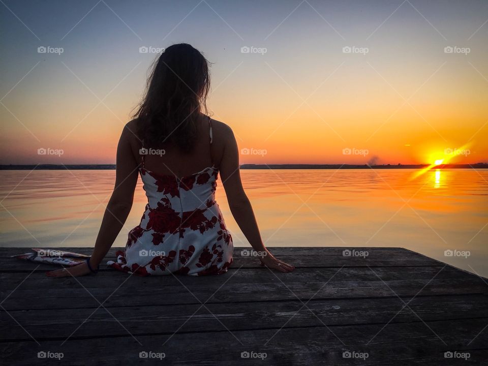 Back of woman wearing summer dress on wooden pontoon watching the sunset over the lake