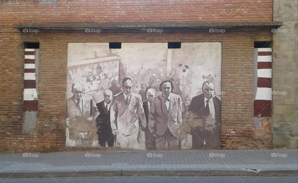 Mural in black and white. Street art on building along the narrow sidewalk.