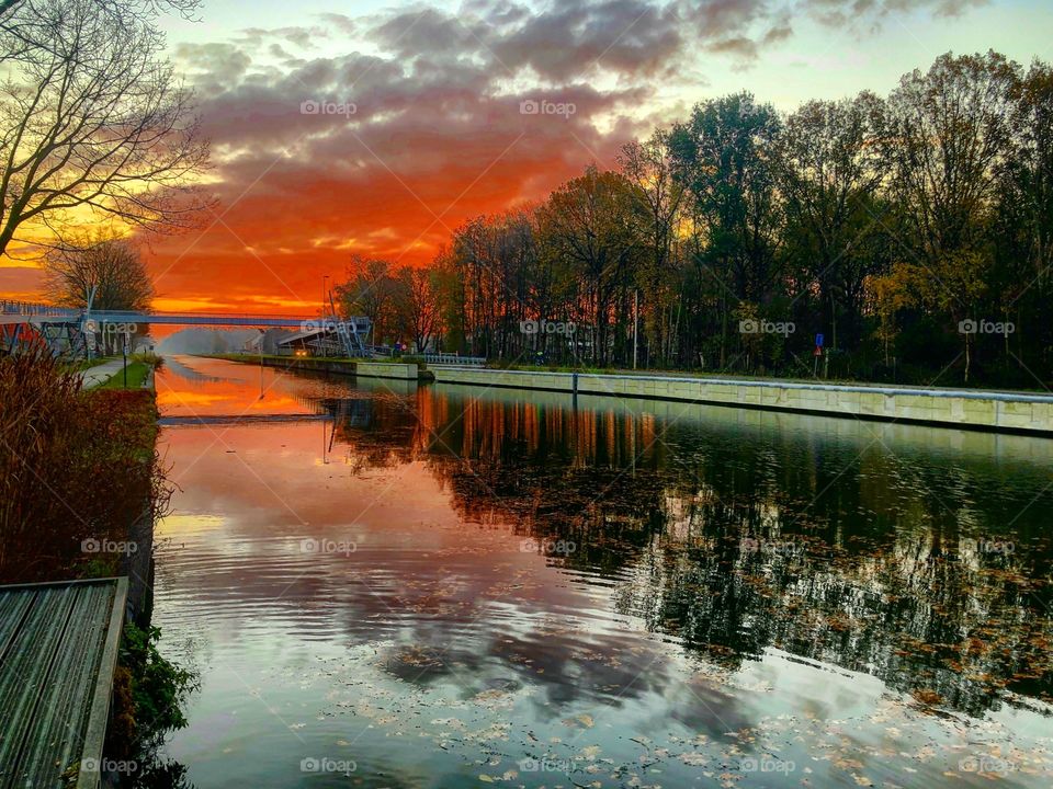 Fiery red sky at dawn reflected in the water of the river in a Countryside landscape 