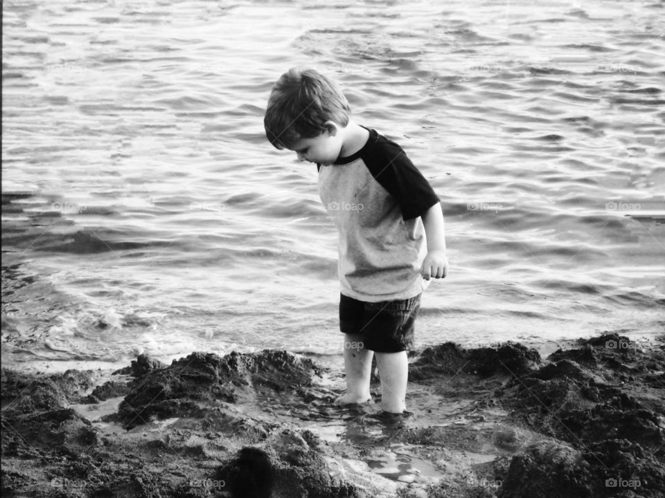 Little boy standing at beach in mud