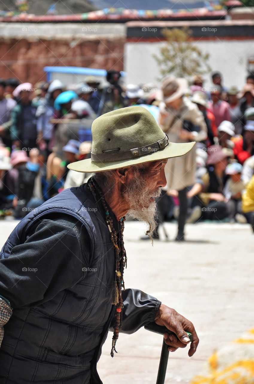 old man in a hat walking in the yard of buddhist monastery in yibet