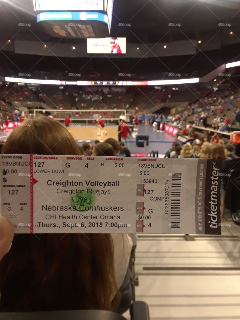 College volleyball game ticket displayed in focus with the crowd and volleyball game blurred in the background