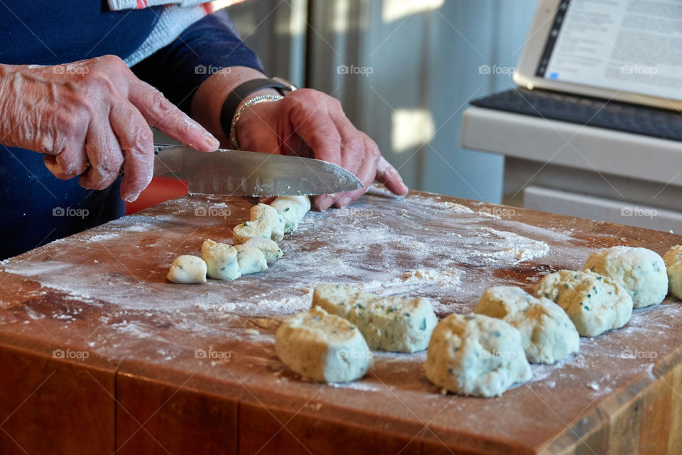 Tech-savvy old woman’s hands make and cut fresh gnocchi in her kitchen on a floured butcher block. Shows skill, fresh ingredients, finely-honed skills, and cooking with love.