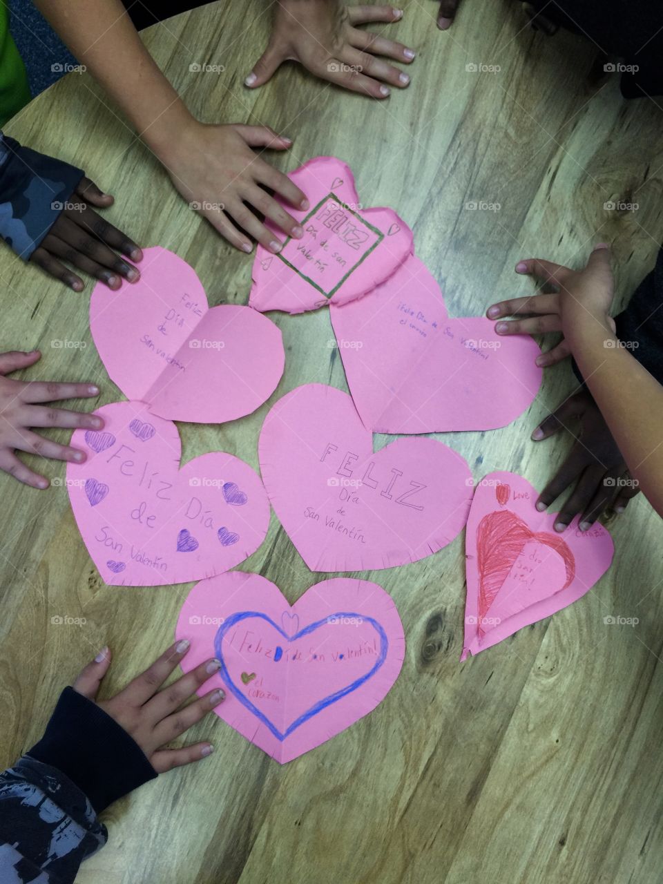Multiple pink paper handmade hearts for Valentine’s Day surrounded by children’s hands