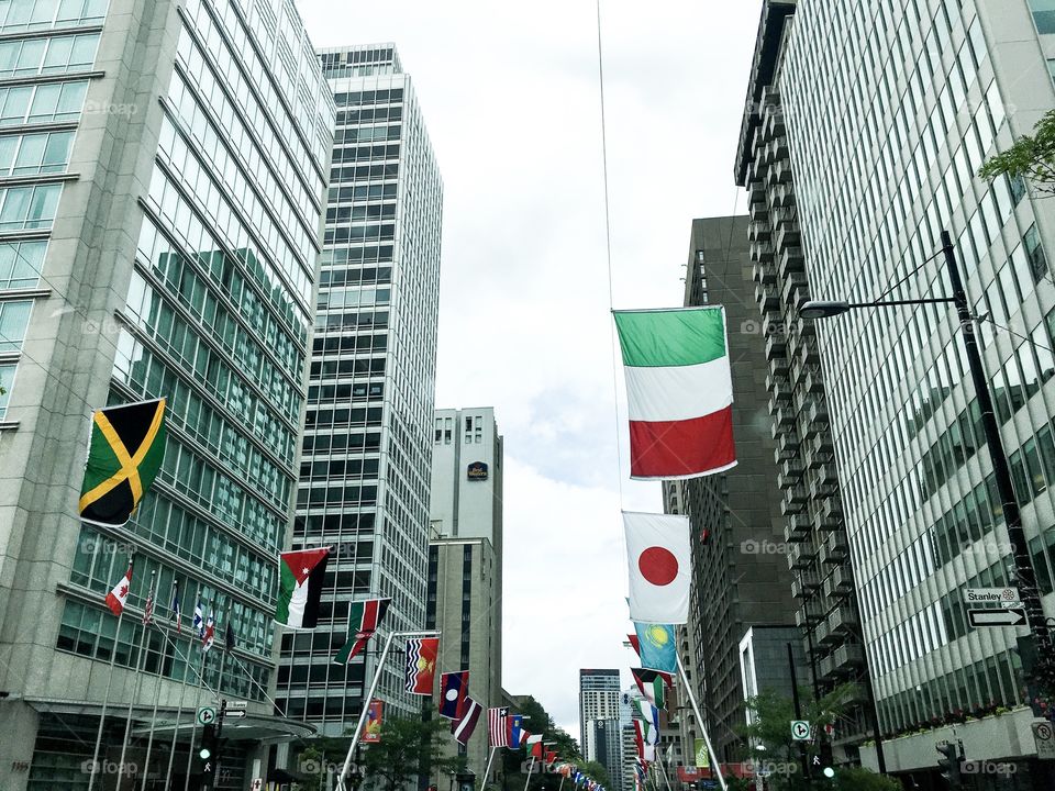 International flags flying in sky against background of tall modern buildings lined up in rows on the streets of downtown Montreal symbolic of culture, diversity and unity and our global business environment 