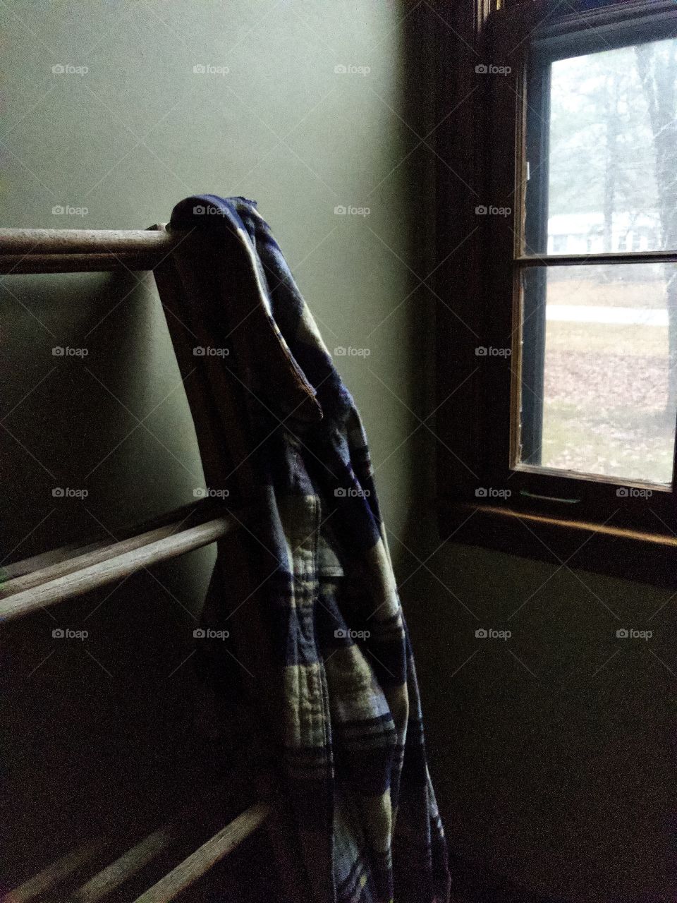 Blue plaid flannel shirt hanging on wooden clothes rack by window 