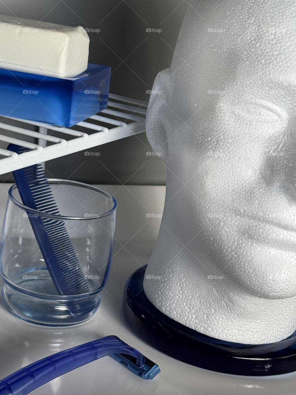 Male white styrofoam head with blue razor and blue glass with comb with blue soap dish and white soap on wire shelf