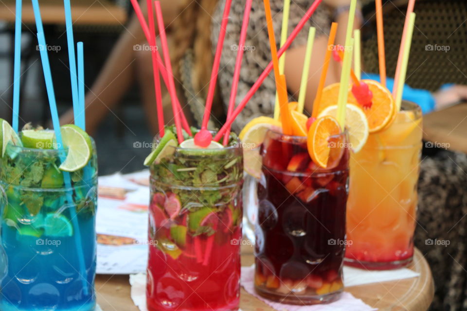 Glasses with colourful cocktails with fruits and herbs inside and straws on top 