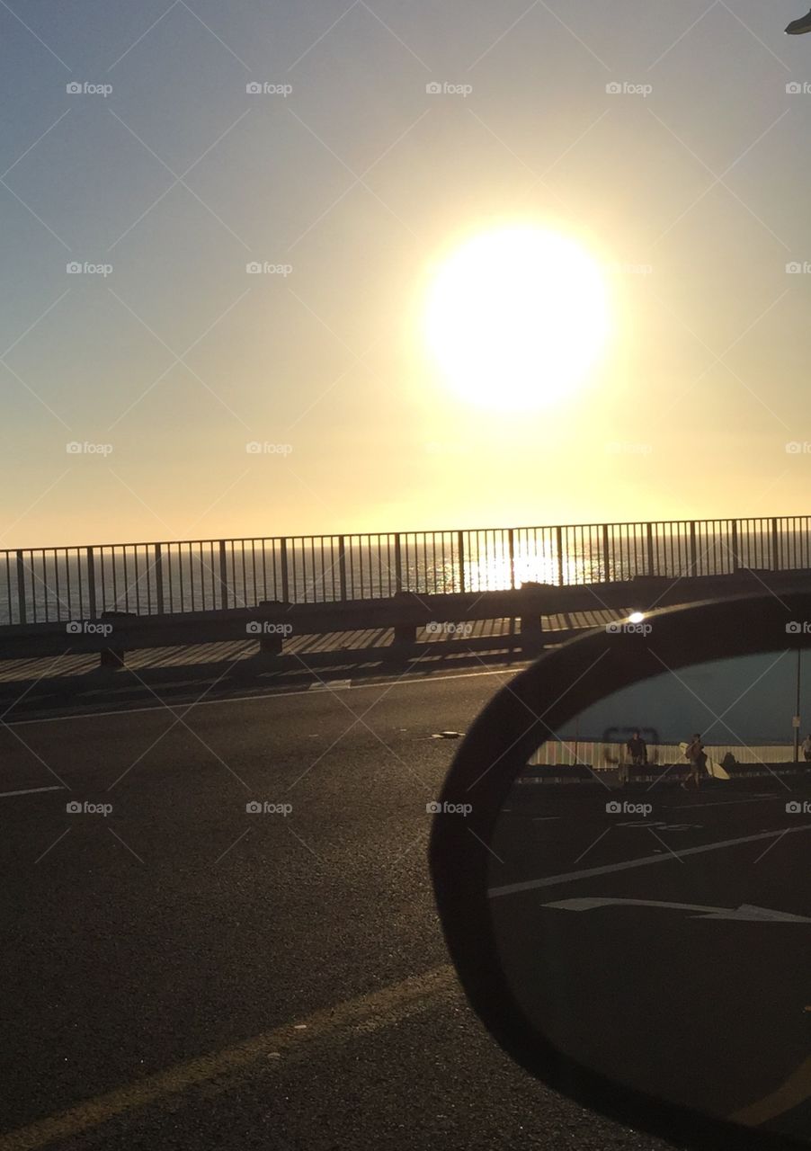 Surfer walking with board . Just a chance photo of the setting sun with a surfer walking with a surf board in the rear view mirror.