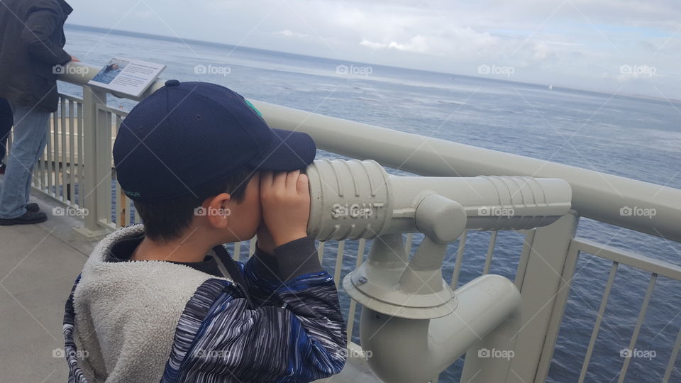 boy looking at ocean through telescope
