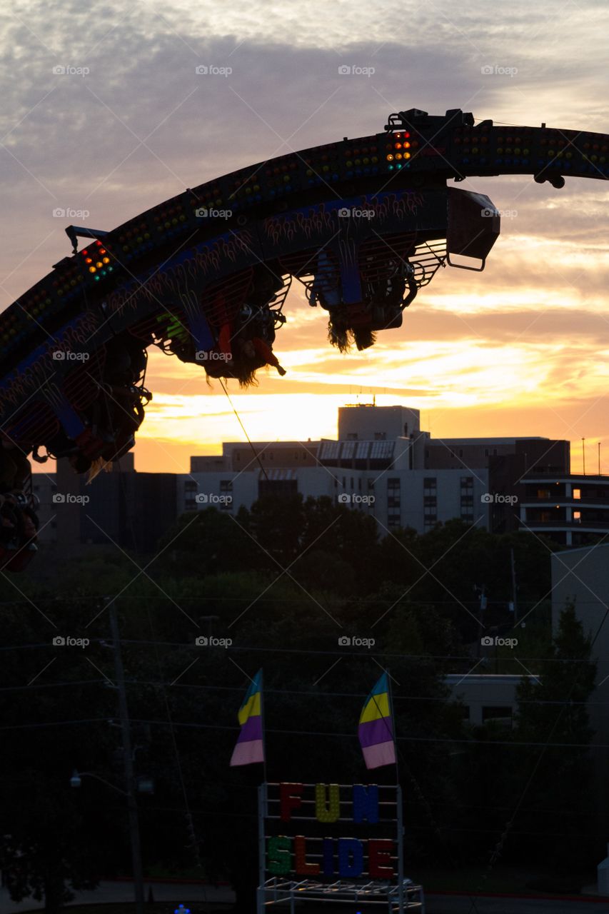 People upside down in amusement park ride silhouetted against sunset 