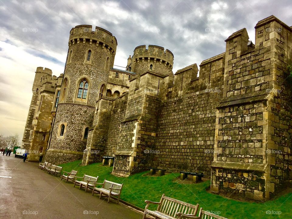 A section of Windsor Castle, looking over the oath and green lawn on a cloudy day