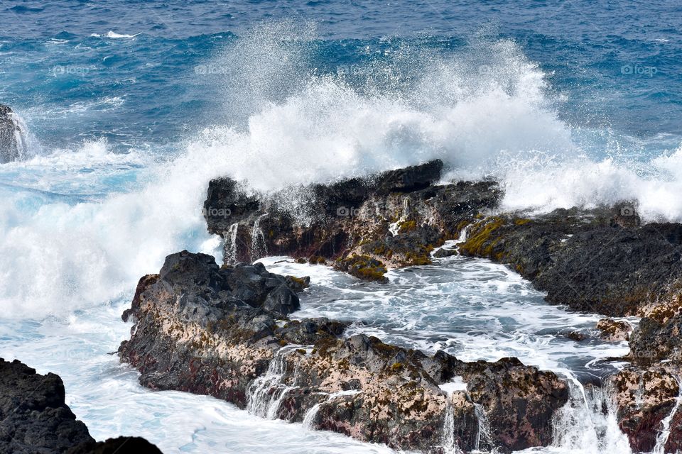 An ocean wave hits an outcropping of lava for a big splash.