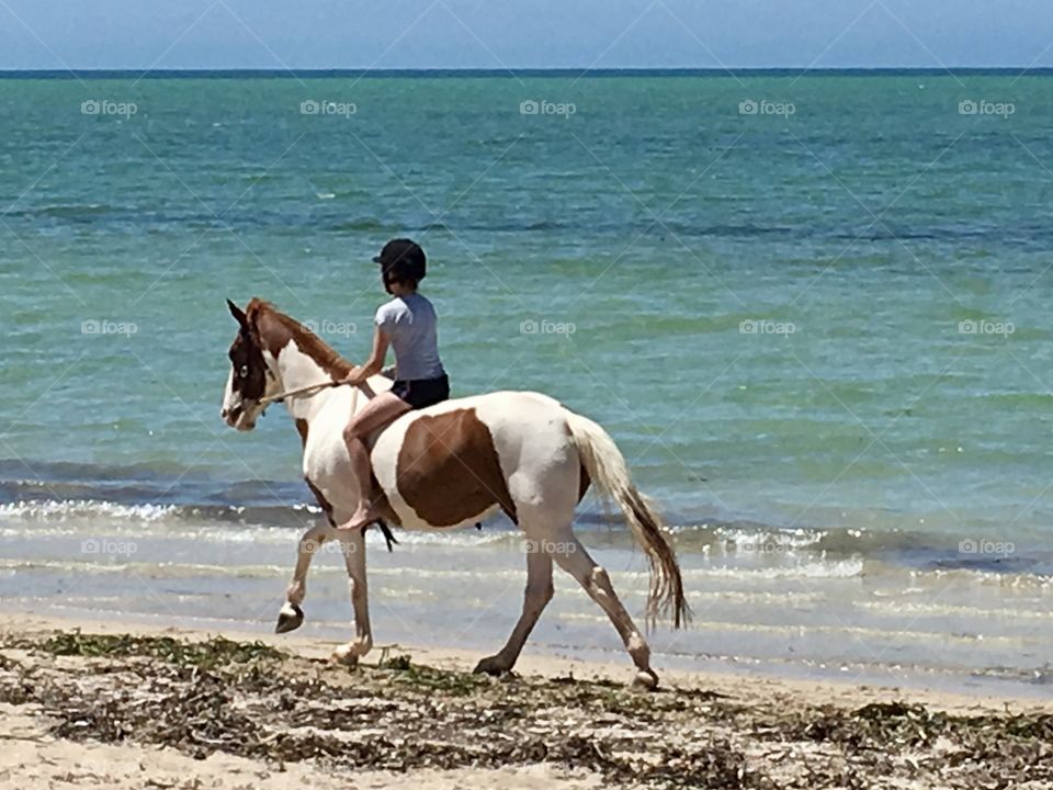 Barefoot girl in riding helmet and bare feet riding horse along the beach at the ocean 