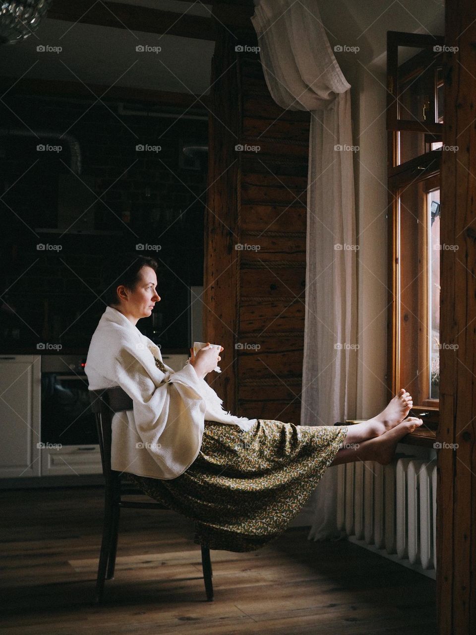 Young beautiful woman with cup sitting near window in cozy home