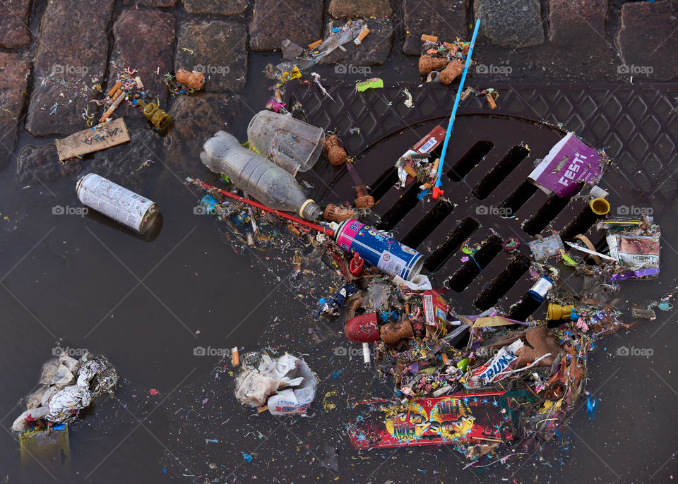 Helsinki, Finland - May 1, 2017: Plastic and other trash over sewer and partly floating in a puddle on cobble street after first of May celebrations.