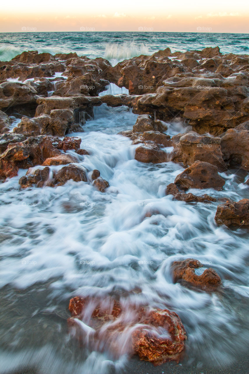 Coral cove in Jupiter Florida, beautiful red rocks on the beach with blue water flowing through them