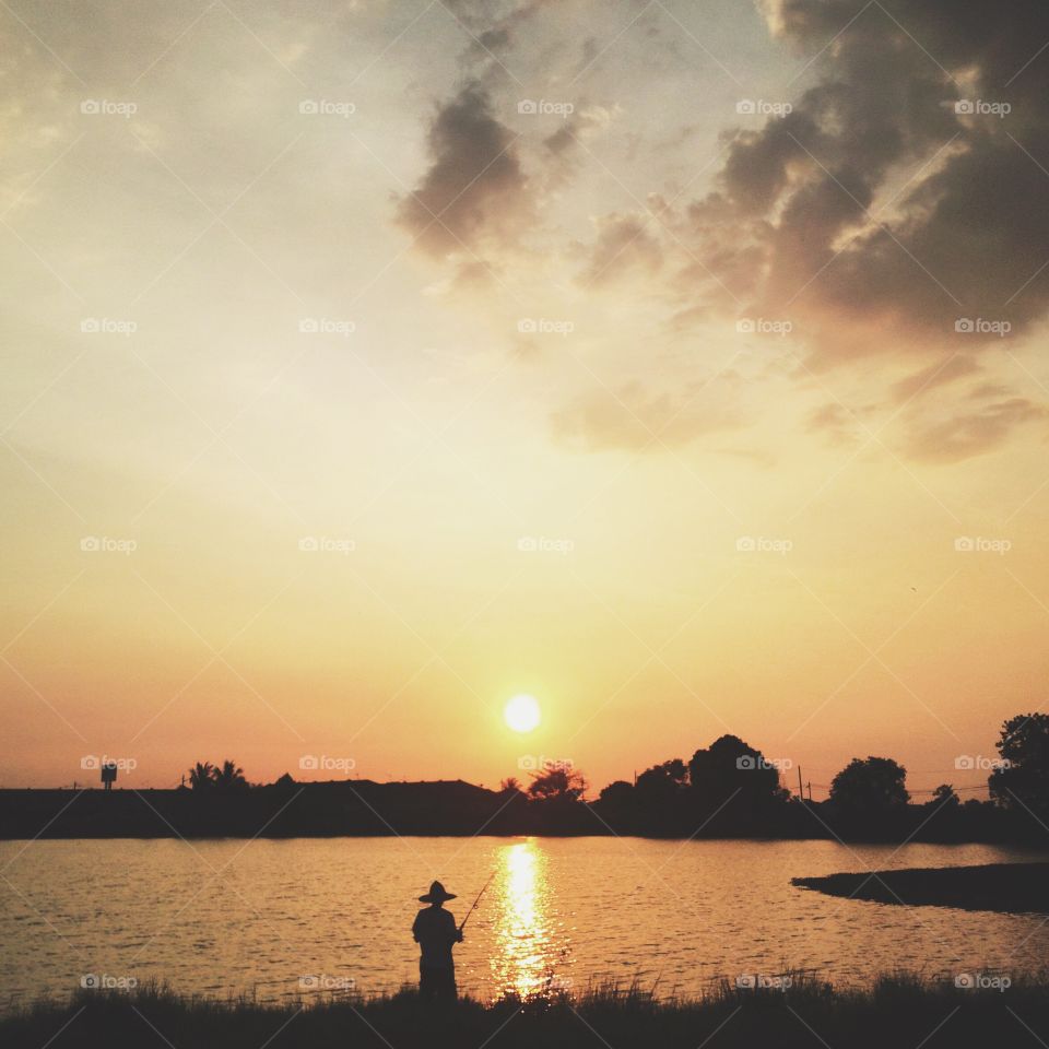 Silhouette of fisherman fishing on lake at sunset