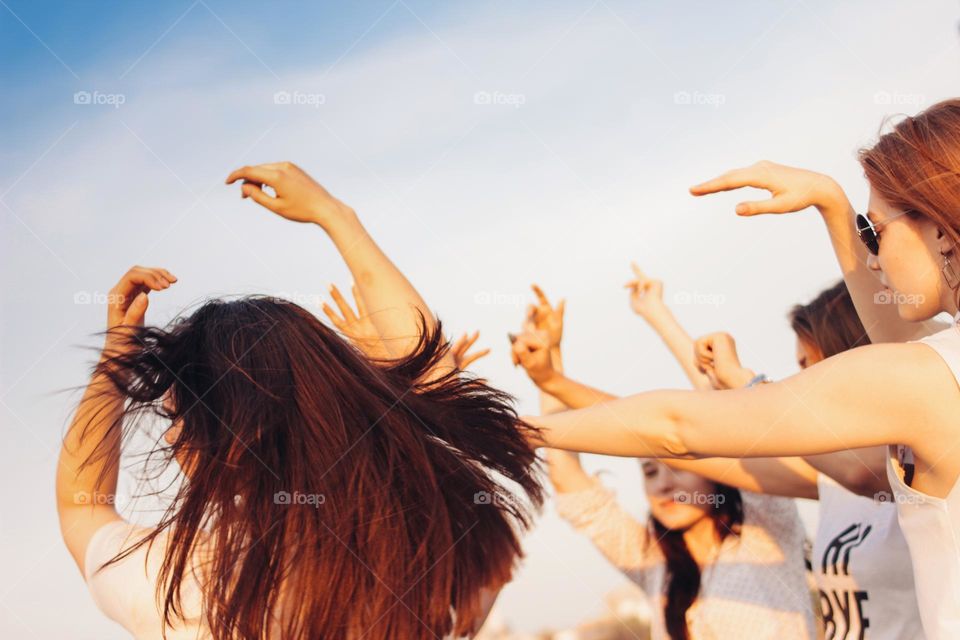 Group of young happy dancing tan girls on blue sky background, summer time, open air party