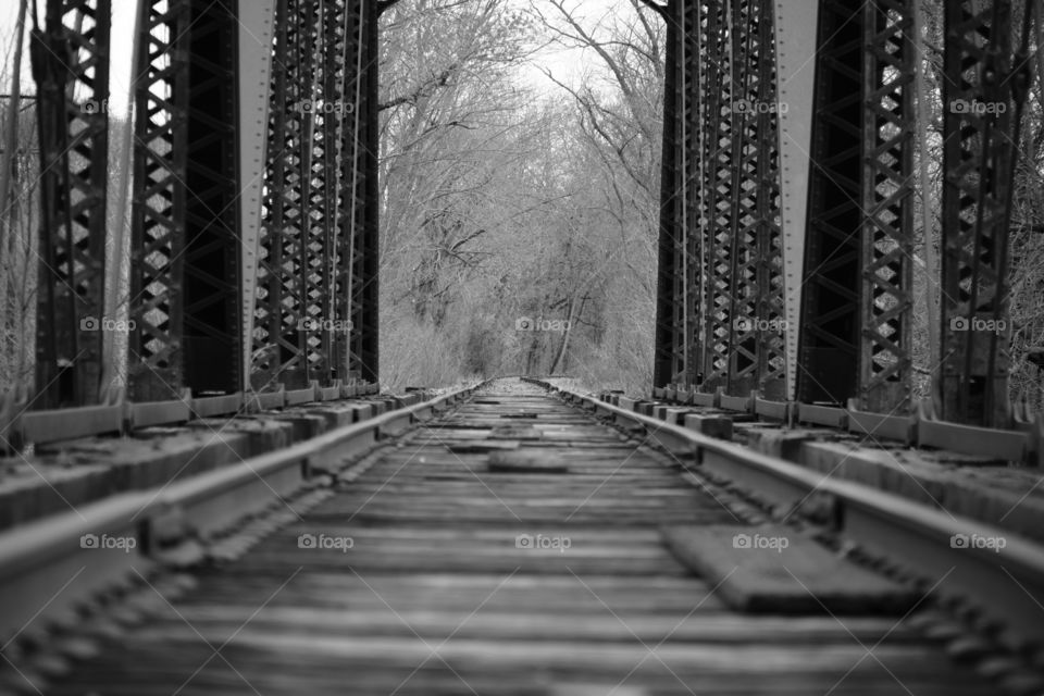 The view down the tracks of a train bridge in black and white. 