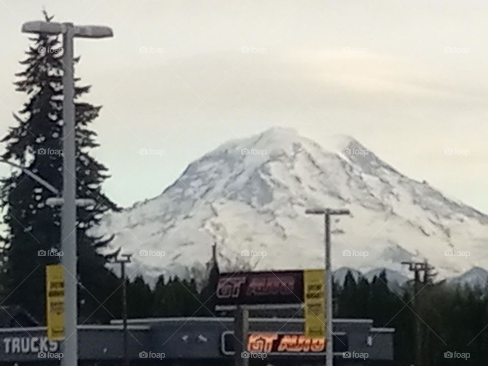 A majestic, snow covered Mt Rainier, graces the background of a small town auto sales business.
