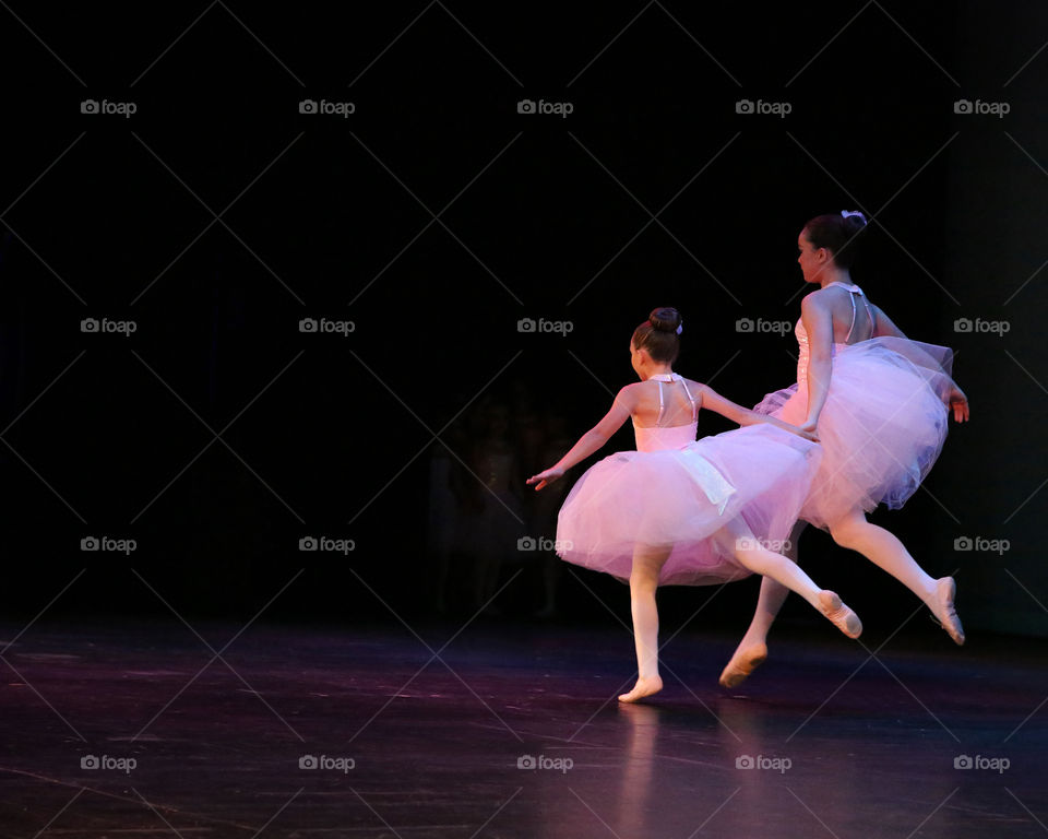 Young female ballet dance duo in pink tutus gracefully crossing stage while holding hands