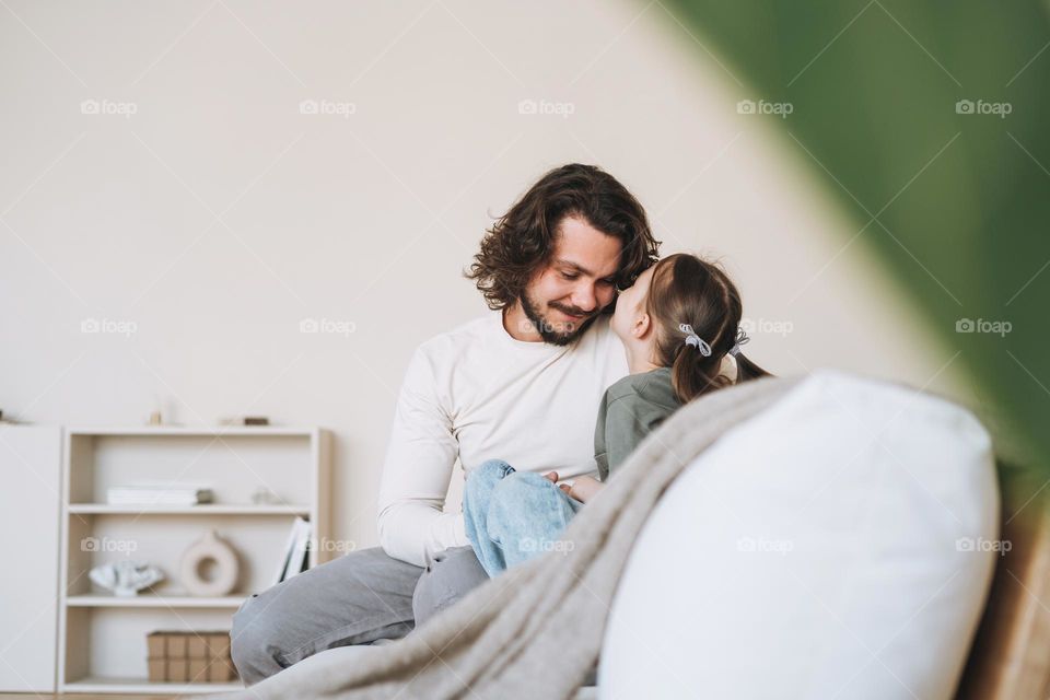 Young happy family with father and daughter on sofa in cozy home, father day