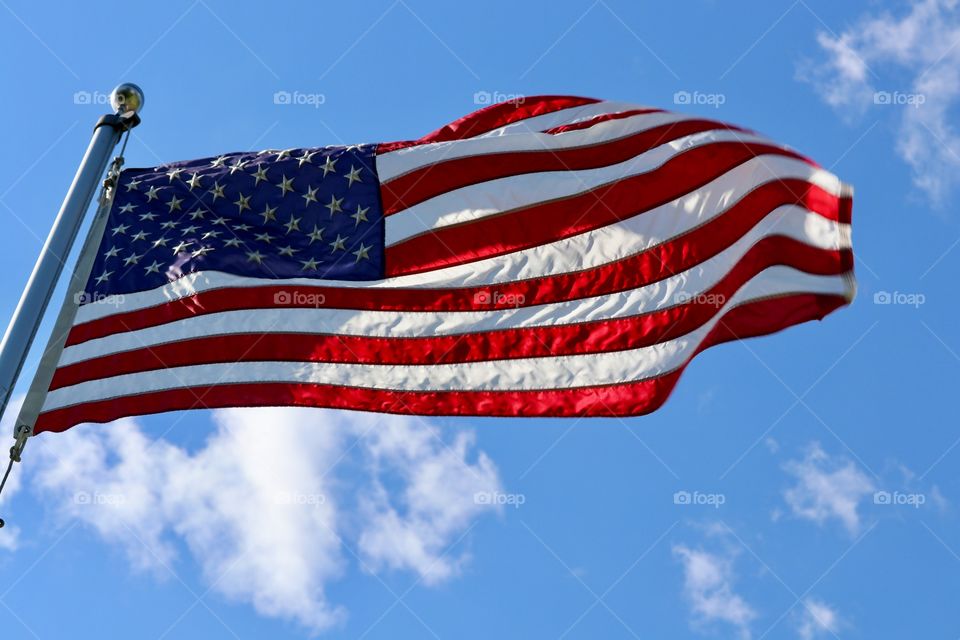 American red white and blue Stars and Stripes flag on flagpole flapping in the wind against a bright vivid blue clear sky suitable for background image 