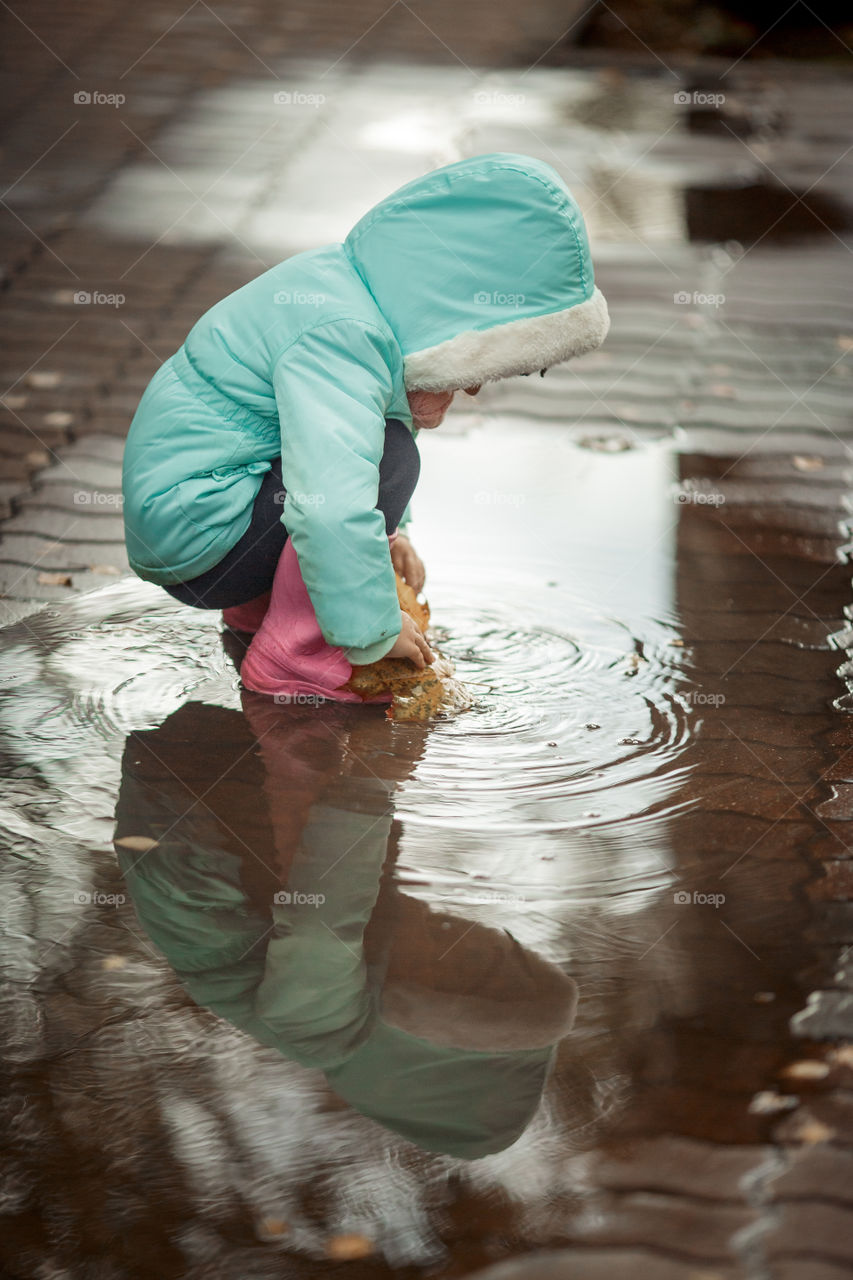 Little girl in rubber boots playing in puddle