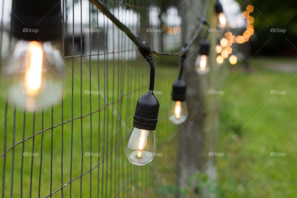 A string of illuminated Edison lights handling along a fence line