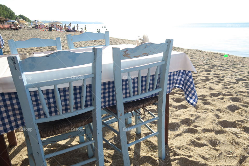 Greek tavern table by the sea. A Greek tavern with tablecloth and chairs just by a sand beach.