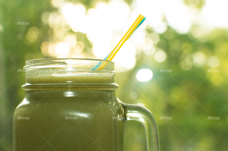 Closeup of sweet fresh basic green fruit smoothie superfoods conceptual background with two straws with trees and setting sun with room for copy 
