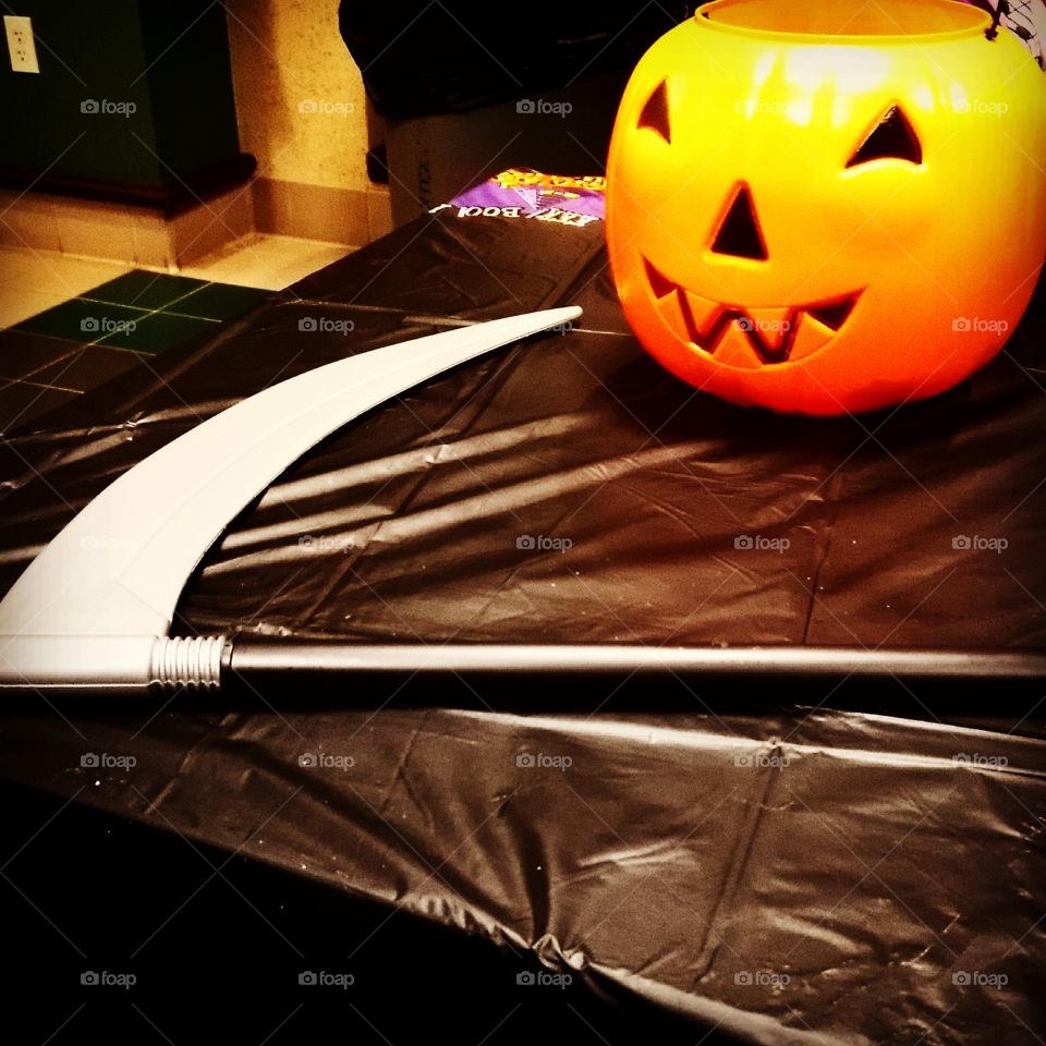 Plastic scythe and pumpkin on black tablecloth