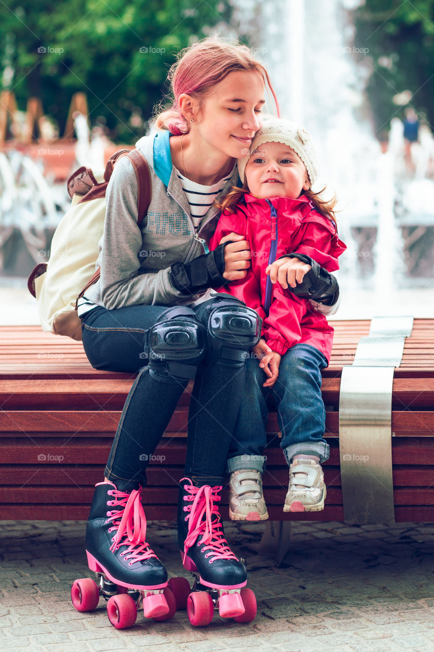 Young girl hugging her little sister while sitting on bench in a city centre
