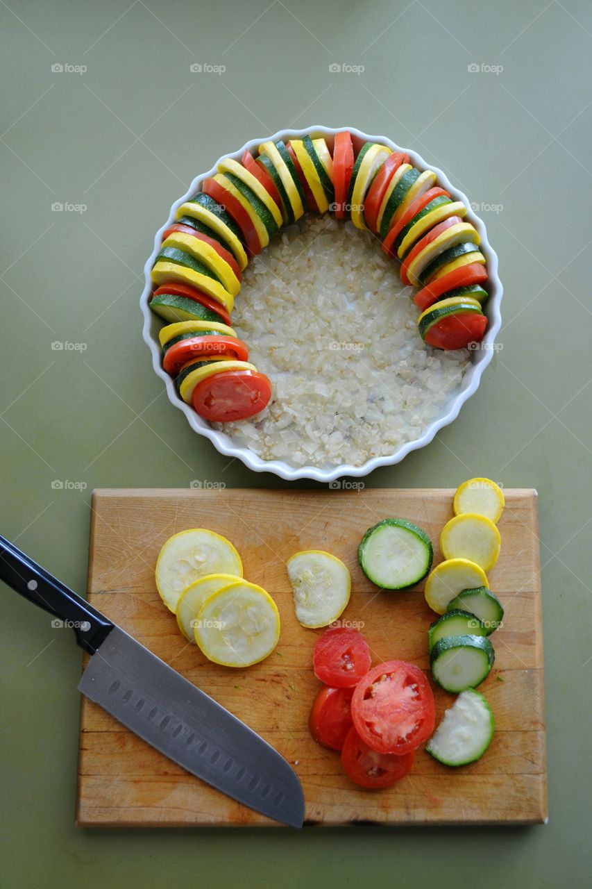 The making of a vegetable tian with summer's end harvest of zucchini, summer squash and tomatoes on a bed of garlic and onions.