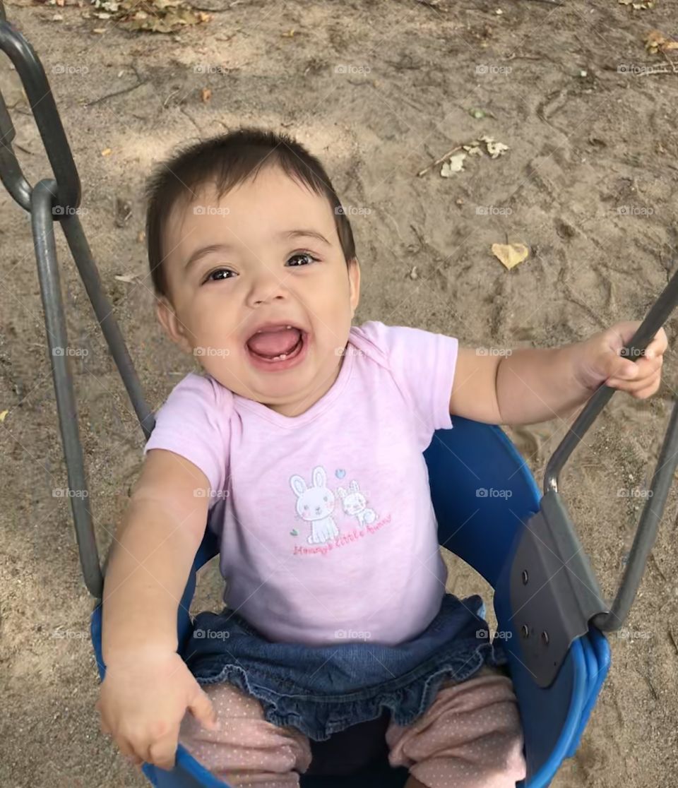 Baby girl smiling and swinging on a park swing