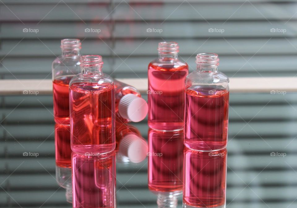 Small glass vials with red liquid on mirror with reflection.  Gray background