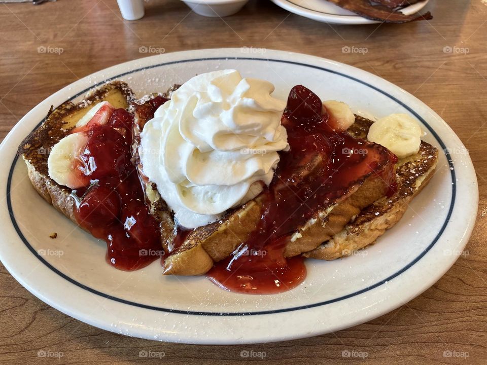 Delicious french toast breakfast with strawberries, bananas, whipped cream and pork sausages
