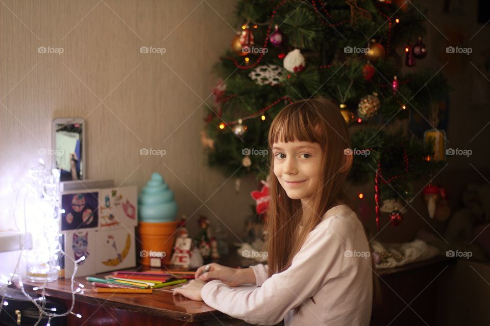 Little girl draws at a table under the Christmas tree